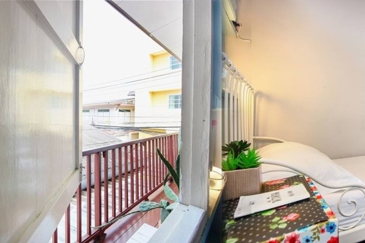 Ein kleines Zimmer mit einem Einzelbett und einem Balkon, ein kleiner Tisch mit einer Pflanze und ein weißes Bett.