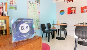 Un comptoir d’accueil d’auberge de jeunesse avec un panneau indiquant une note de 8,8 attribuée par les Guest Review Awards 2016. La pièce contient plusieurs chaises et tables noires.