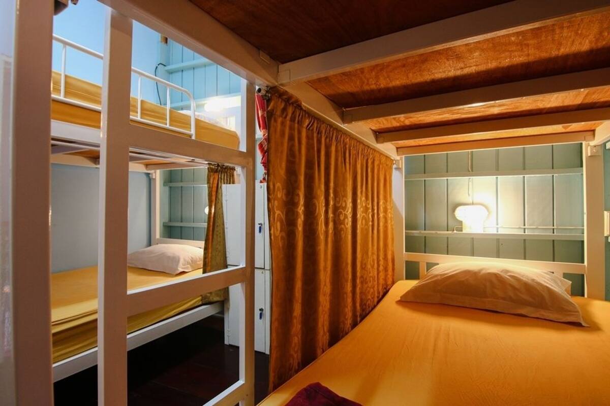 Ein Schlafraum mit Etagenbetten, Holzbalkendecke, einem Fenster mit Vorhängen und einer Nachttischlampe.