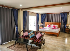 A hotel room with a wooden bed, a glass coffee table, and a sofa with colorful cushions.