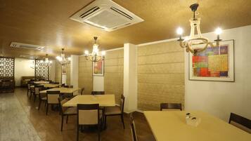 Un restaurante con varias mesas y sillas, ventilaciones en el techo y candelabros fijados a la pared.