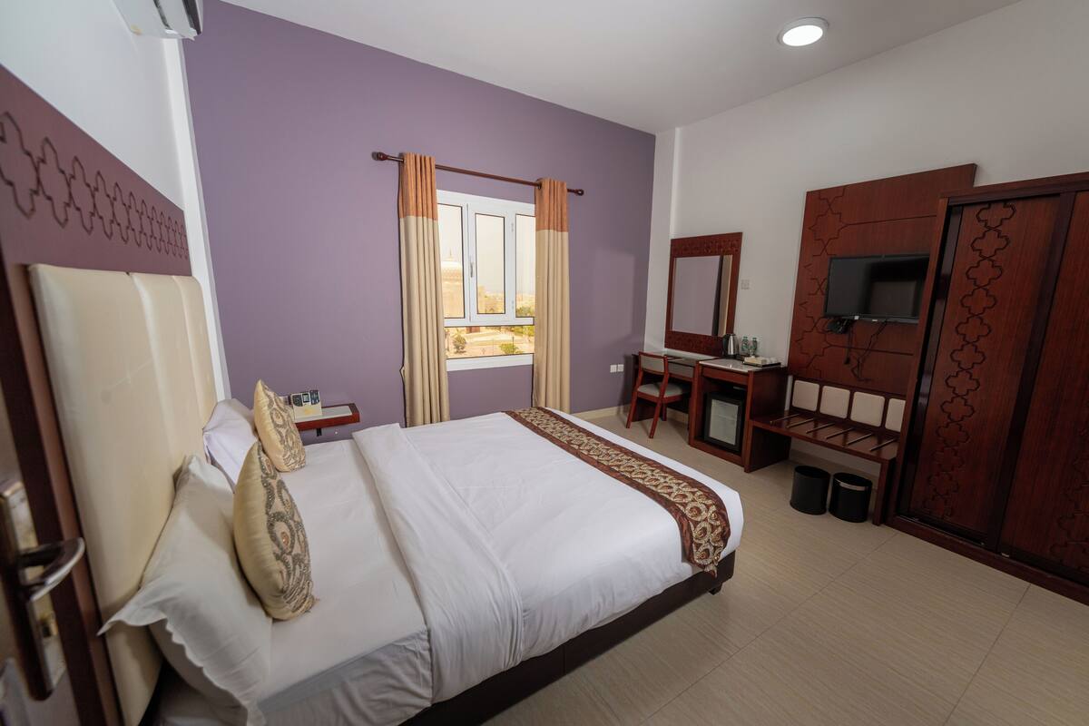 A hotel room with a bed, a desk, a chair, a TV, and a window with curtains.