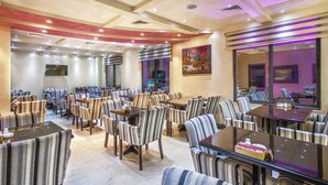 A spacious restaurant with striped chairs and tables, a flat-screen TV mounted on the wall, and a large window offering a view. - Sofia Suites Hotel (Amman)