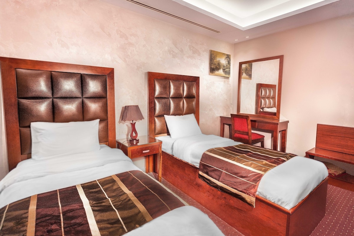 A hotel room with two beds, a wooden headboard, a desk, and a chair.