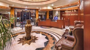 A lobby with a reception desk, a large decorative vase, leather seating, and a star-patterned floor. - Sofia Suites Hotel (Amman)