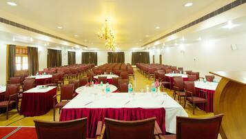 A large conference room with rows of tables and chairs, equipped with water bottles and floral centerpieces.