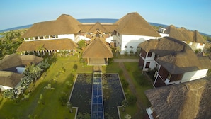 A resort with thatched-roof buildings, a central pool, and a view of the ocean. - Le Pondy Beach & Lake Resort (Puducherry)
