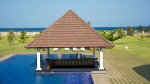 A pool area with a gazebo, a clear view of the beach, and a well-maintained lawn. - Le Pondy Beach & Lake Resort (Puducherry)