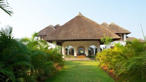 A resort with thatched-roof buildings, a central courtyard, and lush greenery. - Le Pondy Beach & Lake Resort (Puducherry)