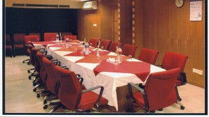 Un salón de conferencias con una mesa larga, sillas rojas y un reloj en la pared.