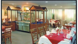 Un comedor con mesas dispuestas para el servicio, sillas de madera y una estación de buffet.