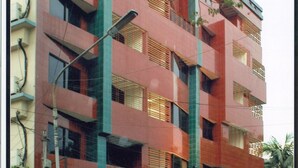 Un edificio de varios pisos con fachada roja, balcones y un espacio comercial en la planta baja.