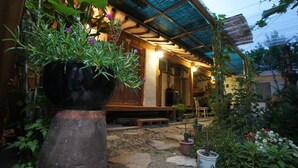 A traditional wooden house with a covered porch, potted plants, and a stone pathway. - 1928 Suimmaru Hanok Guesthouse (Jeonju)