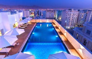 A rooftop pool with lounge chairs and umbrellas, surrounded by high-rise buildings. - Centara Muscat Hotel Oman (Muscat)