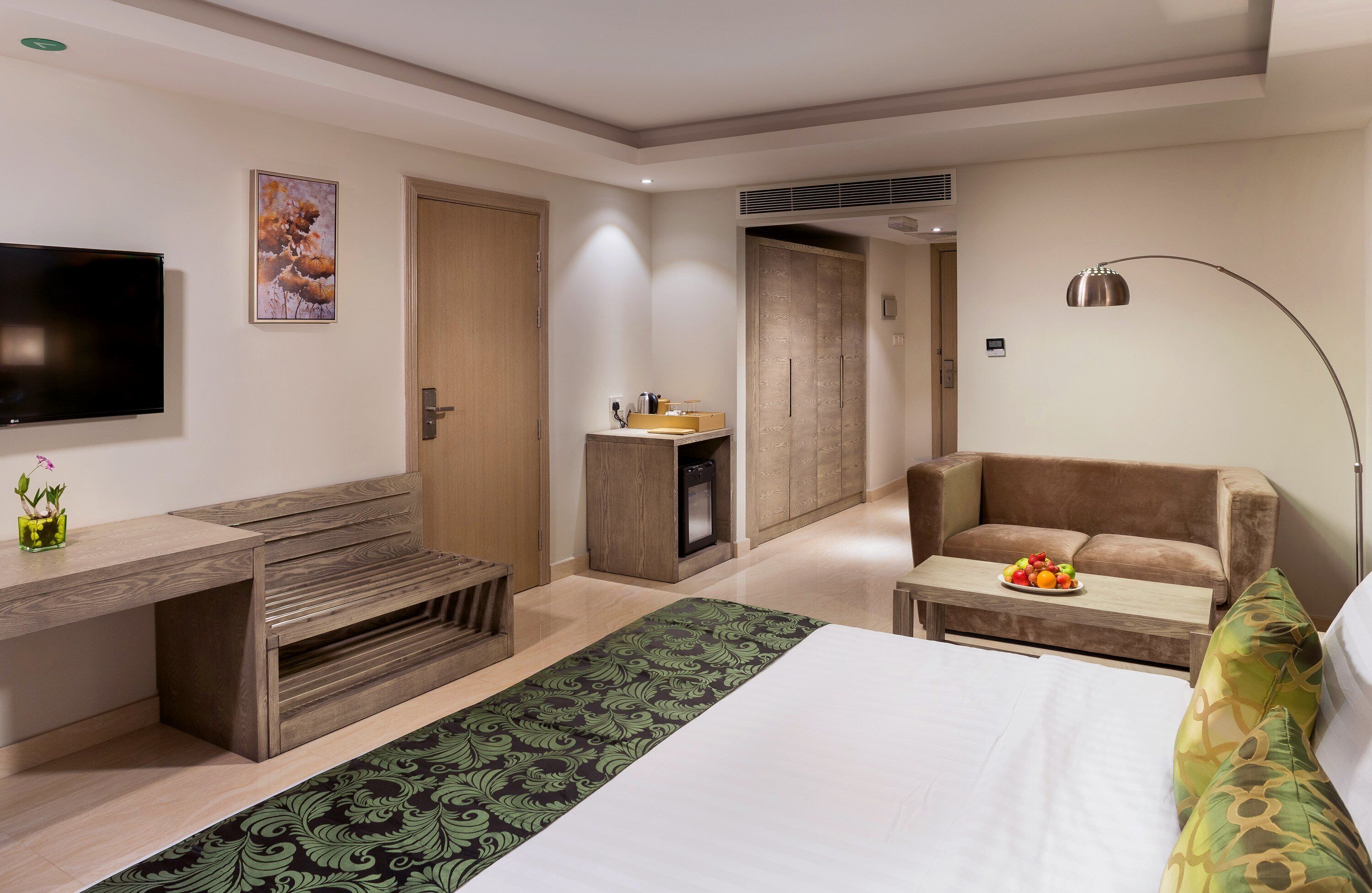 A modern hotel room with a bed, a sofa, a desk, a TV, and a bathroom.