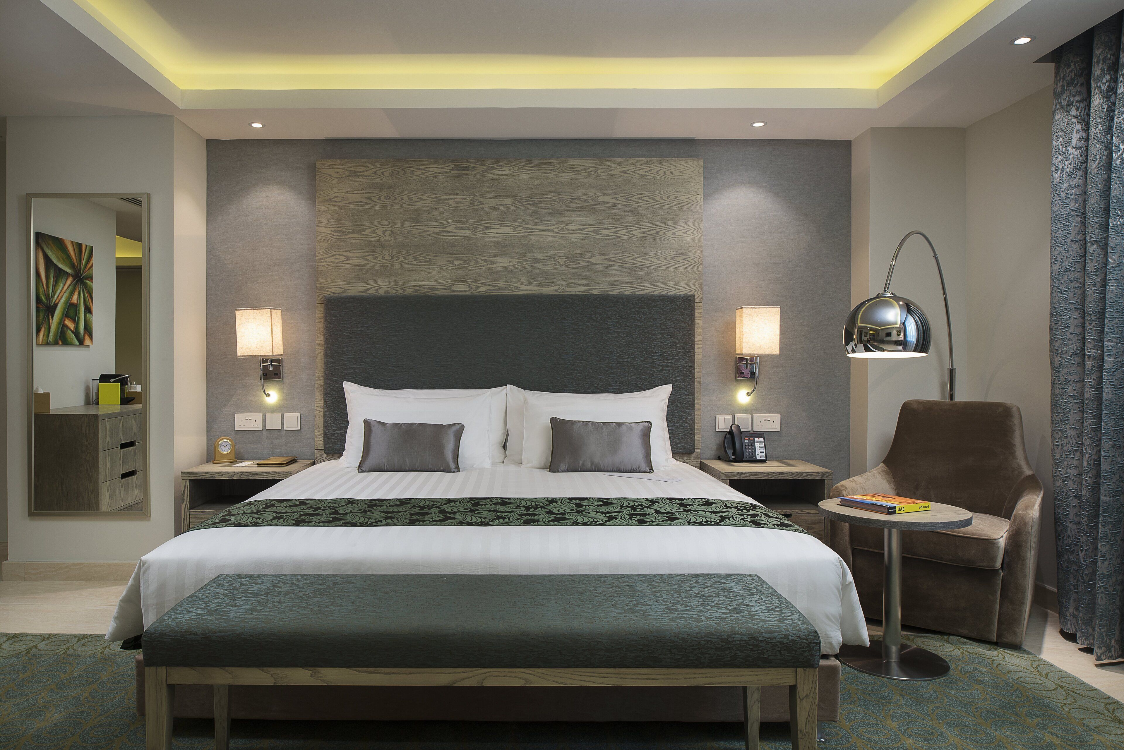 Habitació d'hotel moderna amb un llit gran, làmpades de nit, una cadira i una taula petita.