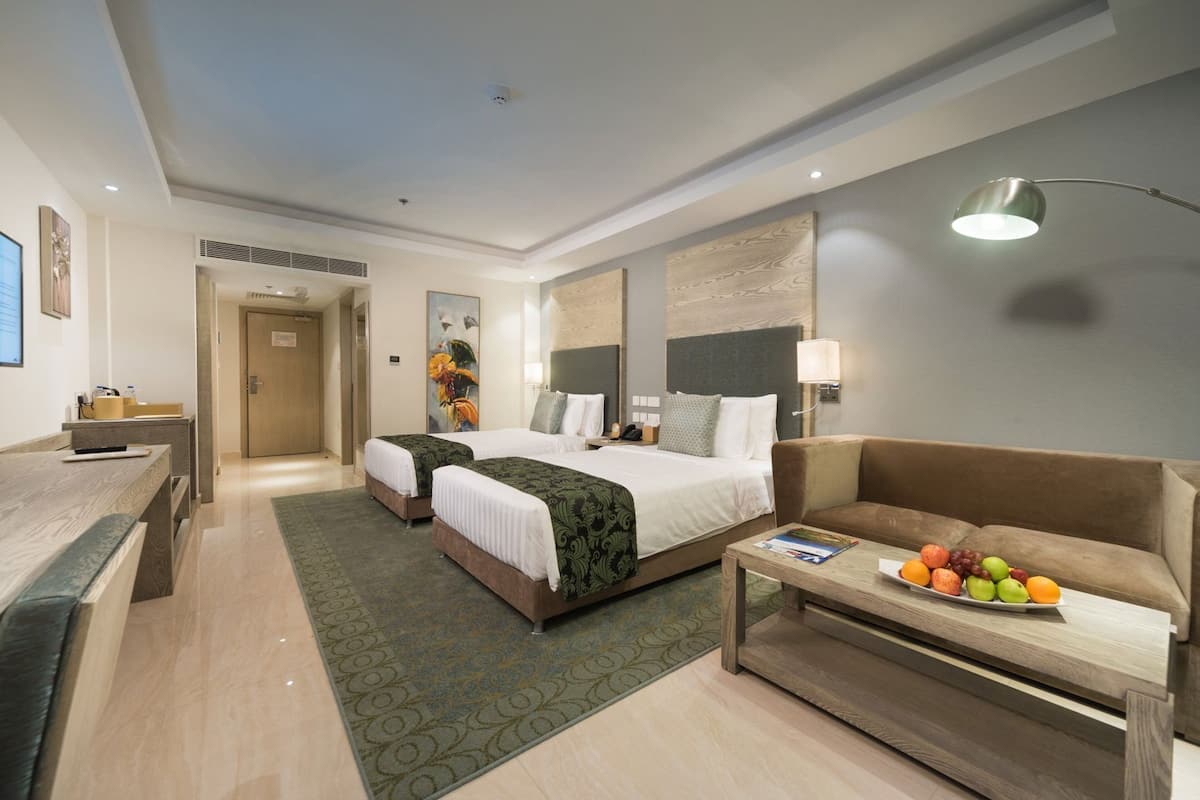 Una habitación de hotel con dos camas, un escritorio, un sofá y un frutero.