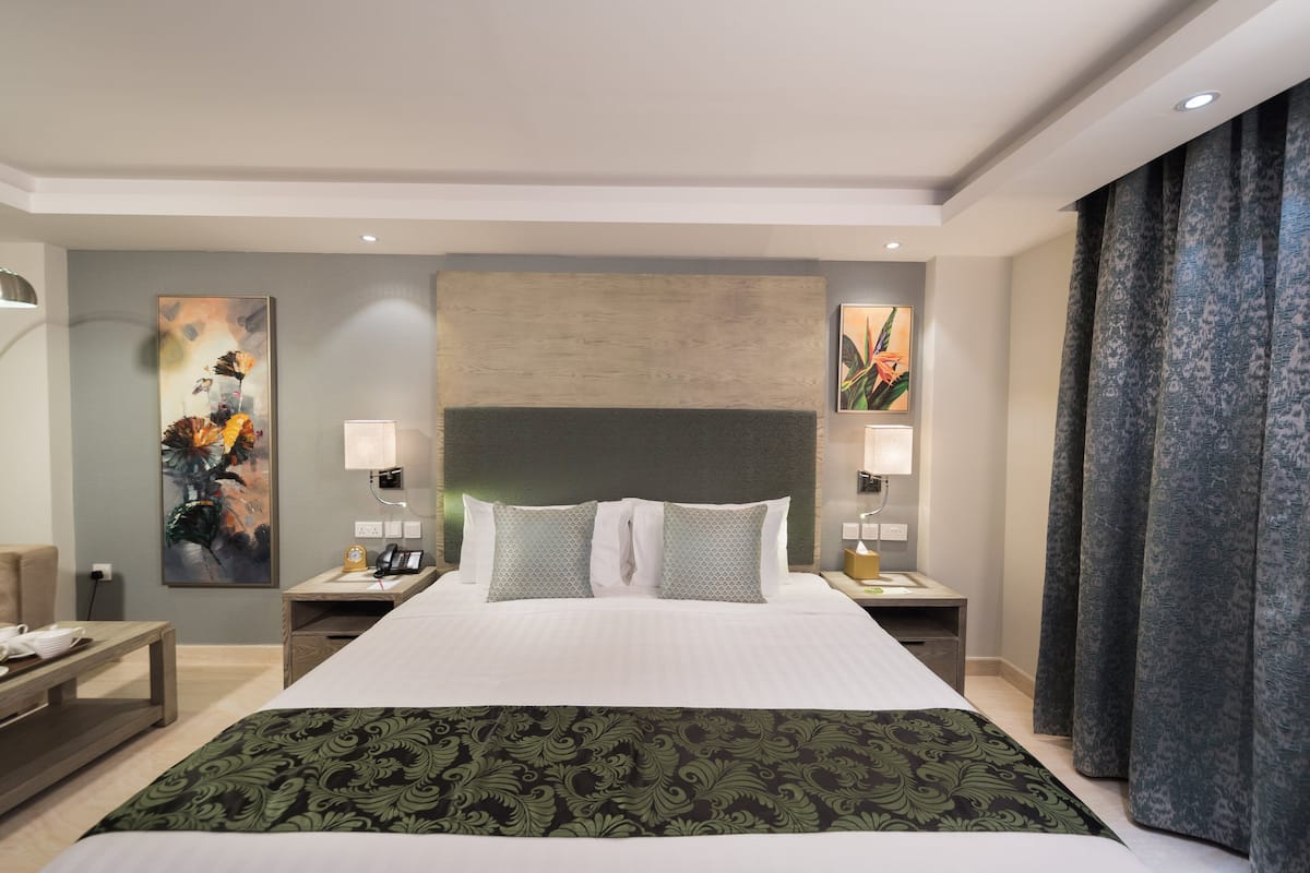 Habitación de hotel con una cama grande, dos mesitas de noche, una lámpara y un cuadro en la pared.