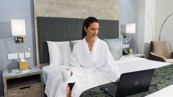 A hotel room with a bed, a nightstand, a lamp, and a laptop on the bed.