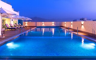 A swimming pool with lounge chairs and umbrellas, surrounded by a tiled deck and a mountain view.
