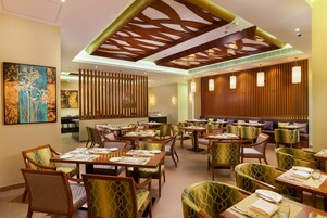 A restaurant with multiple dining tables and chairs, wooden ceiling design, and artwork on the walls.
