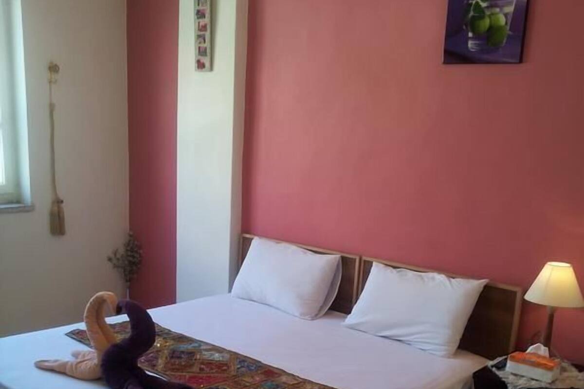 A hotel room with a bed, a nightstand, a lamp, a wall decoration, and a window with curtains.