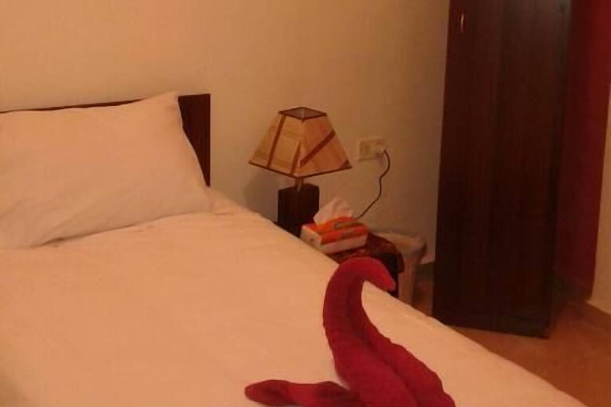 A hotel room with a bed, a nightstand, a lamp, a wardrobe, and a painting on the wall.