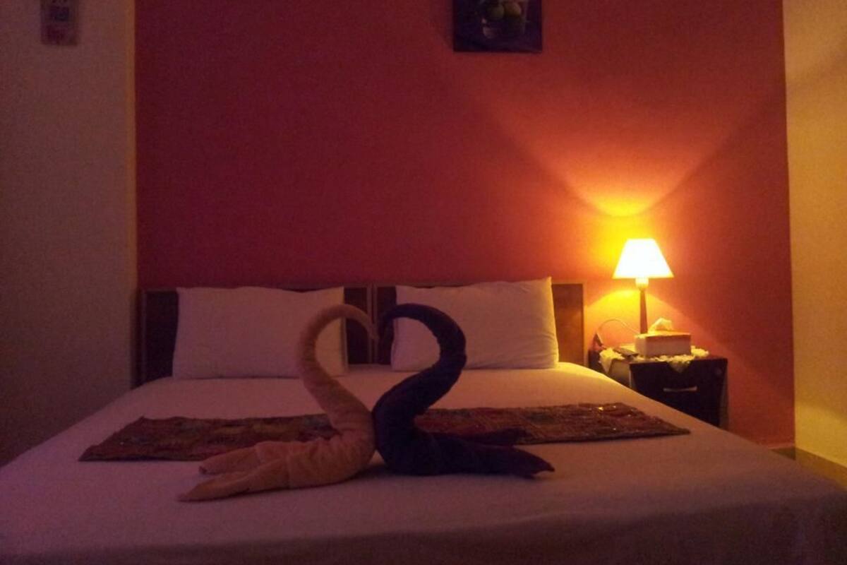 A hotel room with a bed, a nightstand, and a wall-mounted lamp.