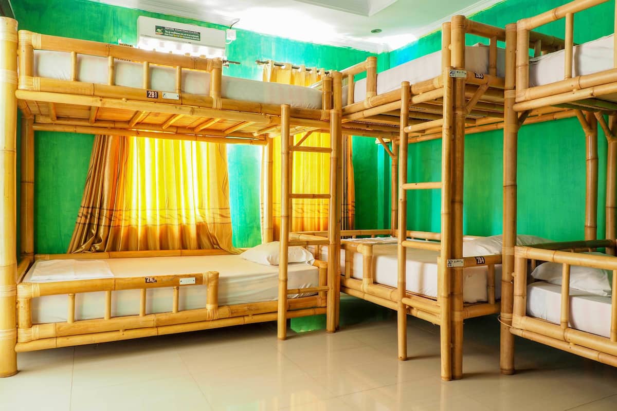 Une chambre avec des lits superposés en bambou, des murs verts et des rideaux.