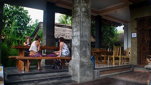 A covered outdoor seating area with stone pillars and wooden benches. - Lagas Hostel (Ubud)