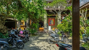 A courtyard with parked motorcycles, a reception area, and lush greenery. - Lagas Hostel (Ubud)