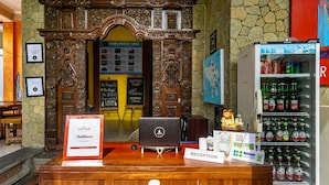 A reception desk with a laptop, a RedDoorz sign, a Coca-Cola refrigerator, and a map on the wall. - Lagas Hostel (Ubud)