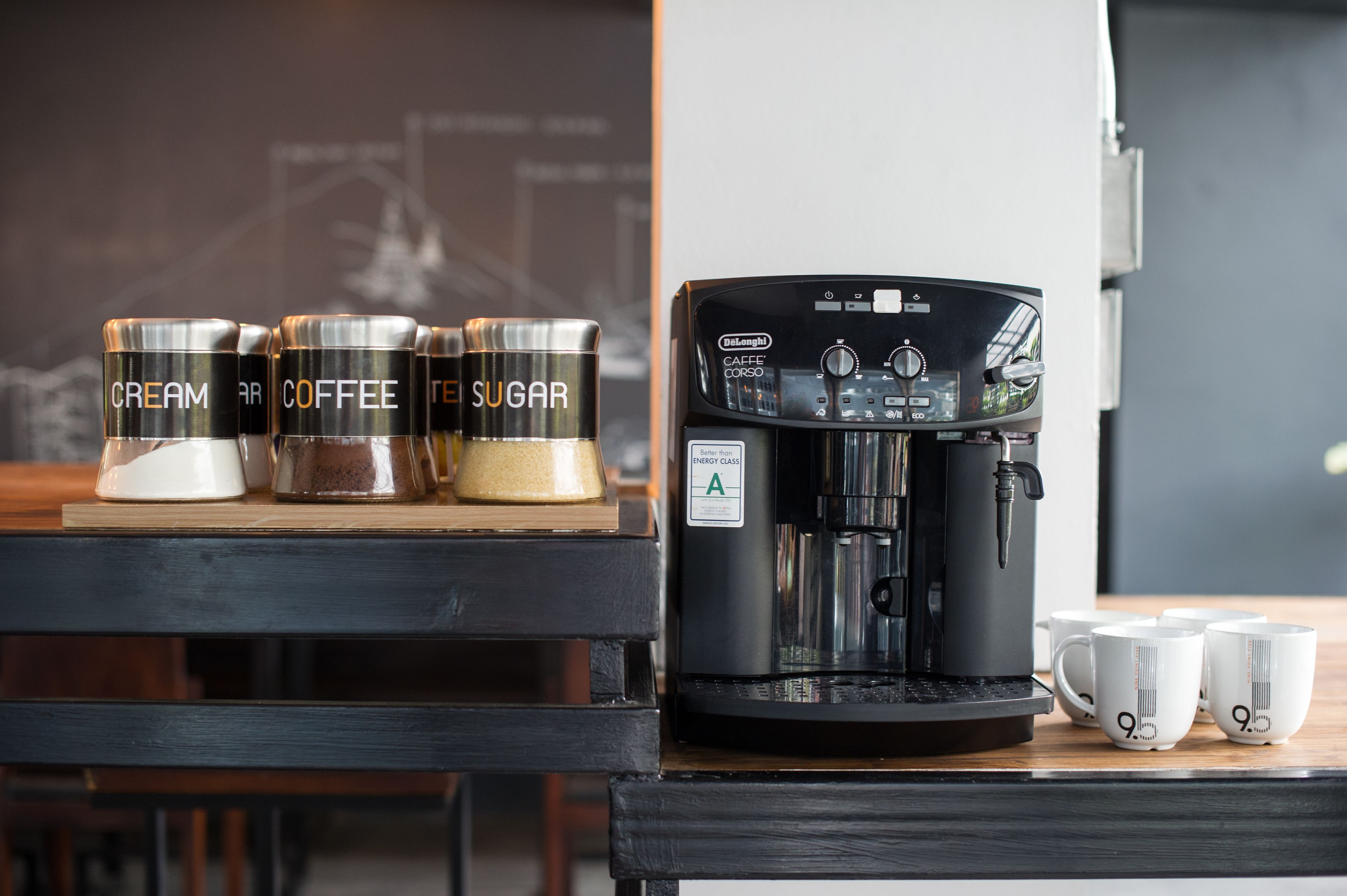 Een koffieapparaat met vier bakjes, gelabeld met room, koffie en suiker, op een houten tafel.