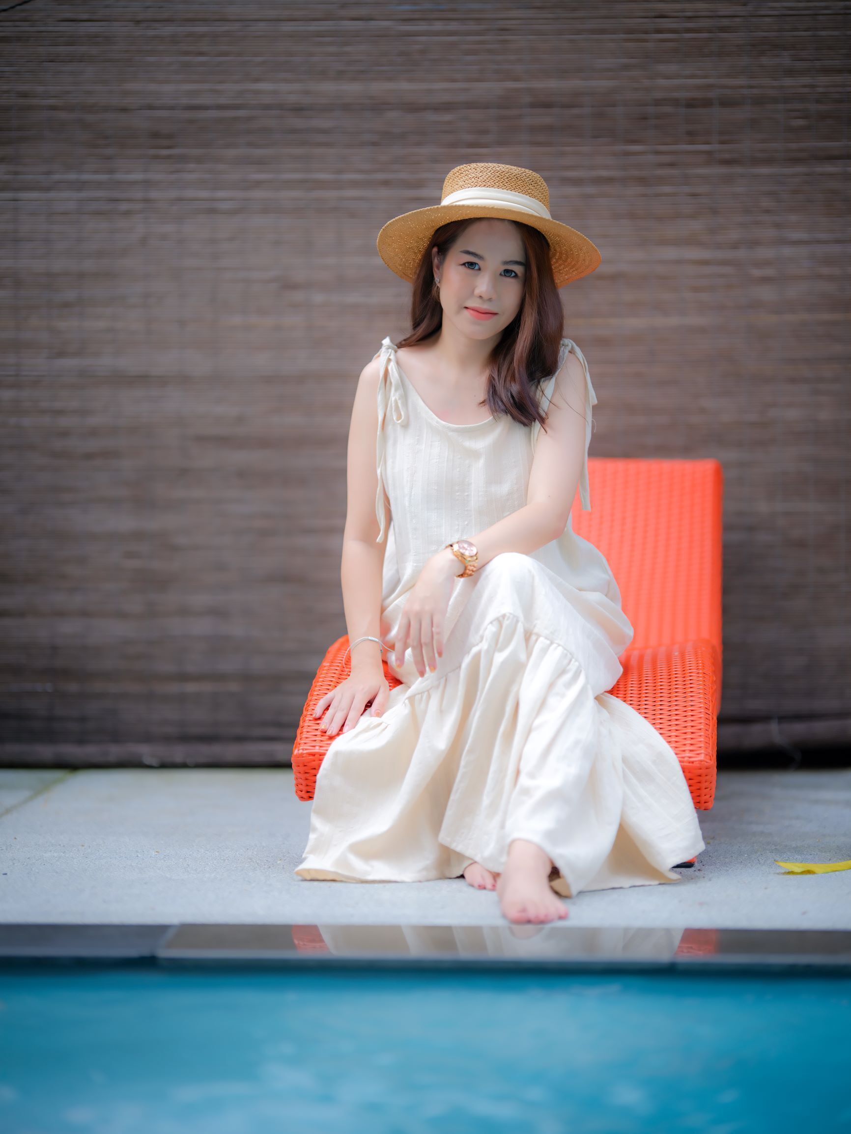 A person sitting on an orange chair by a pool with a wooden wall in the background.