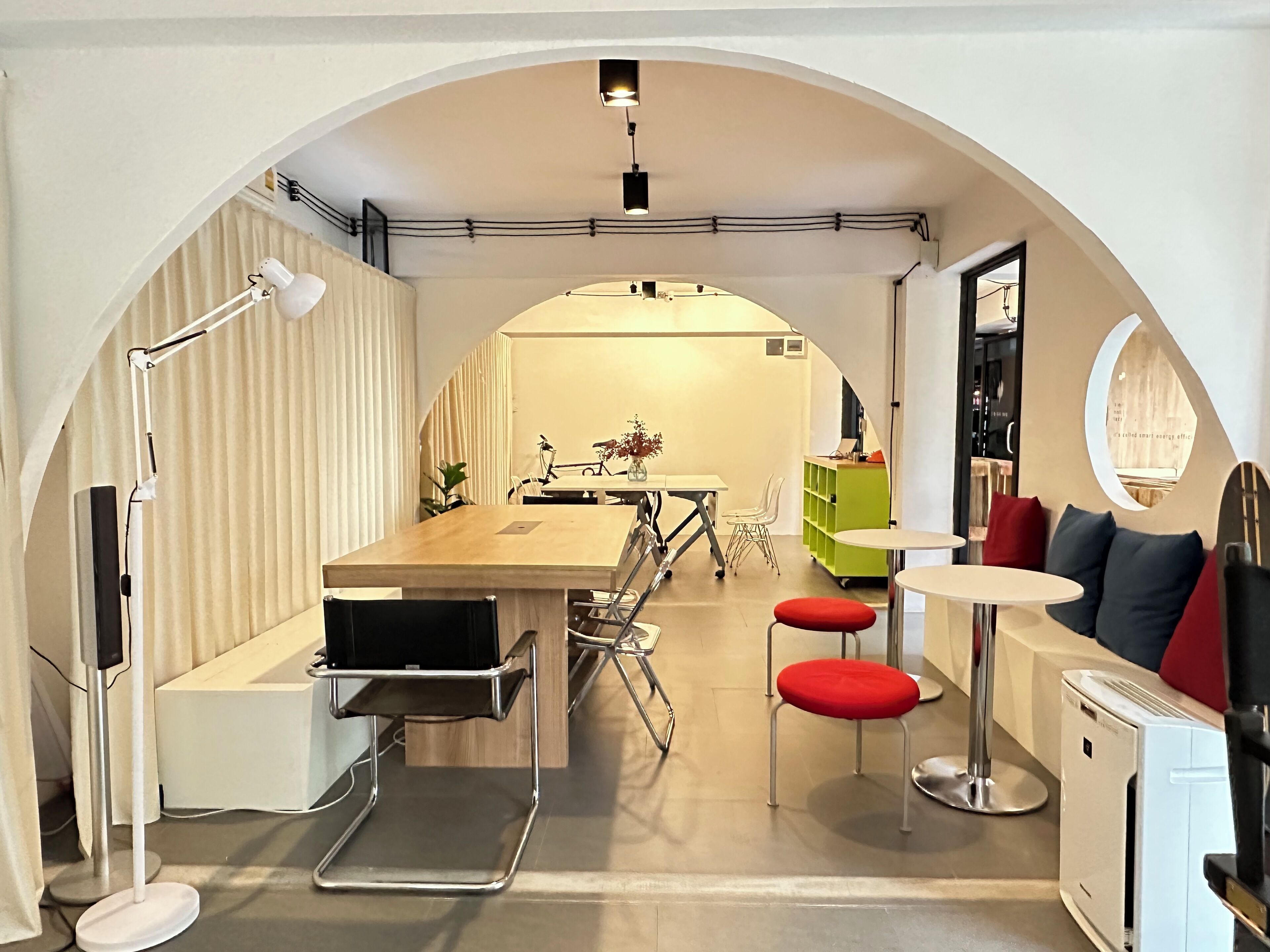 Cozinha compacta e moderna com uma ilha central, área de jantar com mesa e cadeiras, e um pequeno espaço de estar com um banquinho e uma cadeira.