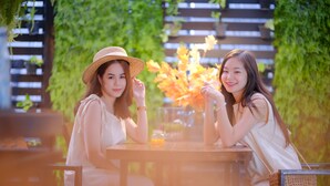 Two people seated at a table outdoors with a wooden fence and greenery in the background. - 9.5 Hotel (Chiang Mai)