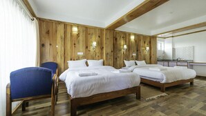 A hotel room with two beds, a chair, wooden walls, and a kitchenette. - Tristar Hotel (Pokhara)