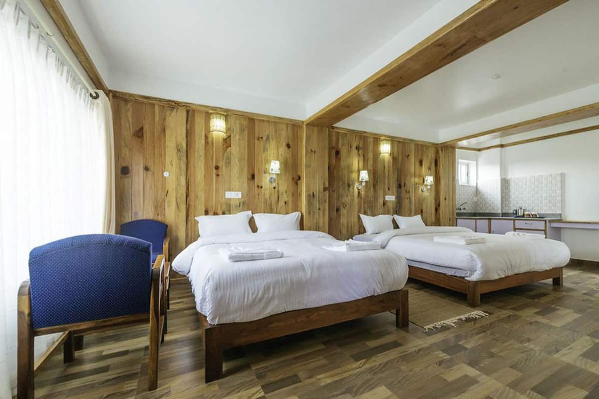 A hotel room with two beds, a chair, wooden walls, and a kitchenette.