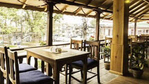 An outdoor seating area with wooden tables and chairs, potted plants, and a view of the street and buildings in the background. - Tristar Hotel (Pokhara)