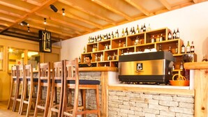 A bar area with wooden chairs, a stone wall, and shelves of bottles. - Tristar Hotel (Pokhara)