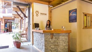 A reception desk with a stone base and a wooden top, a sign reading "TRISTAR," and a framed picture of a flight on the wall. - Tristar Hotel (Pokhara)