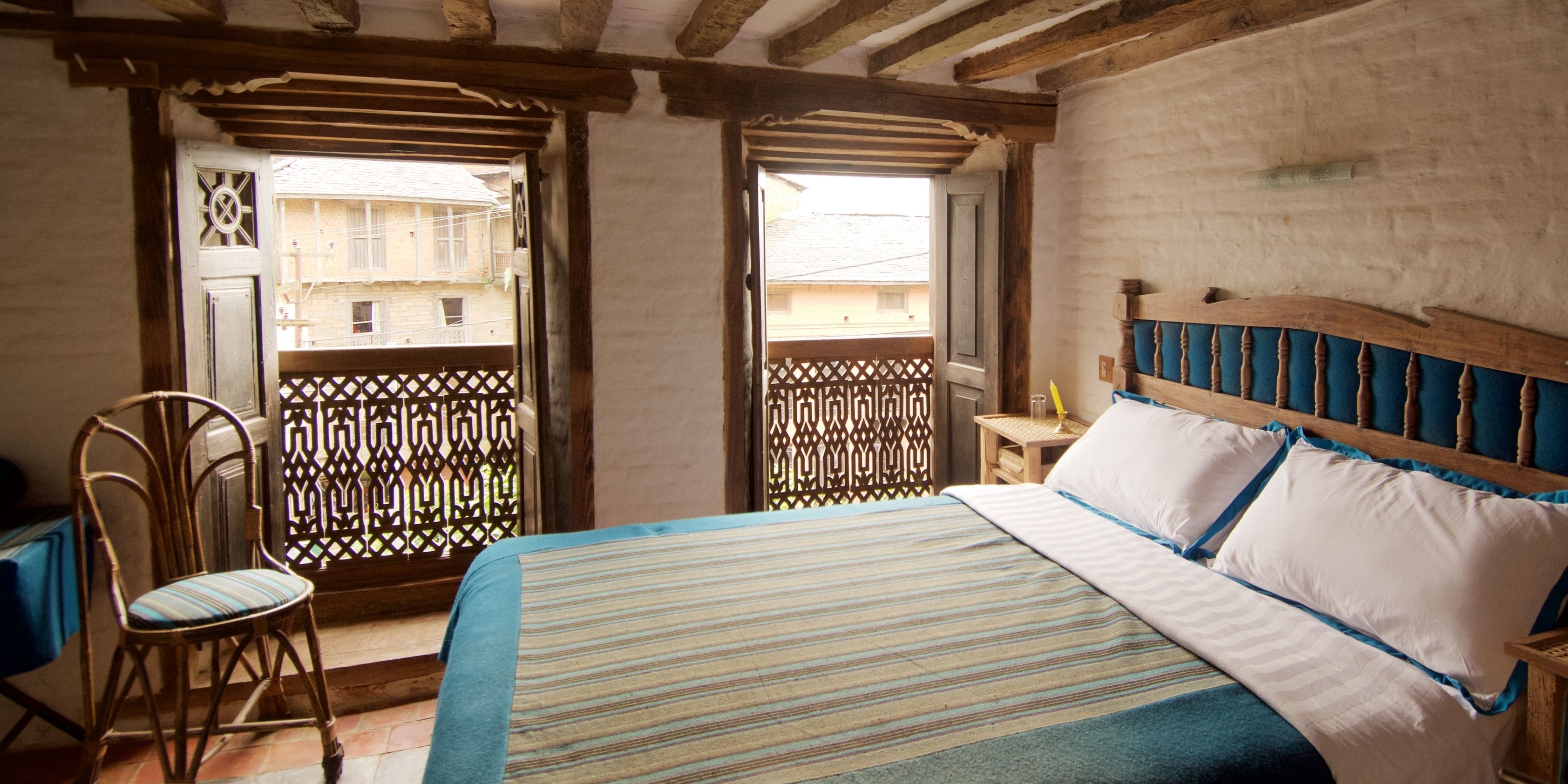A bedroom with a bed, a chair, and a balcony with a lattice fence.