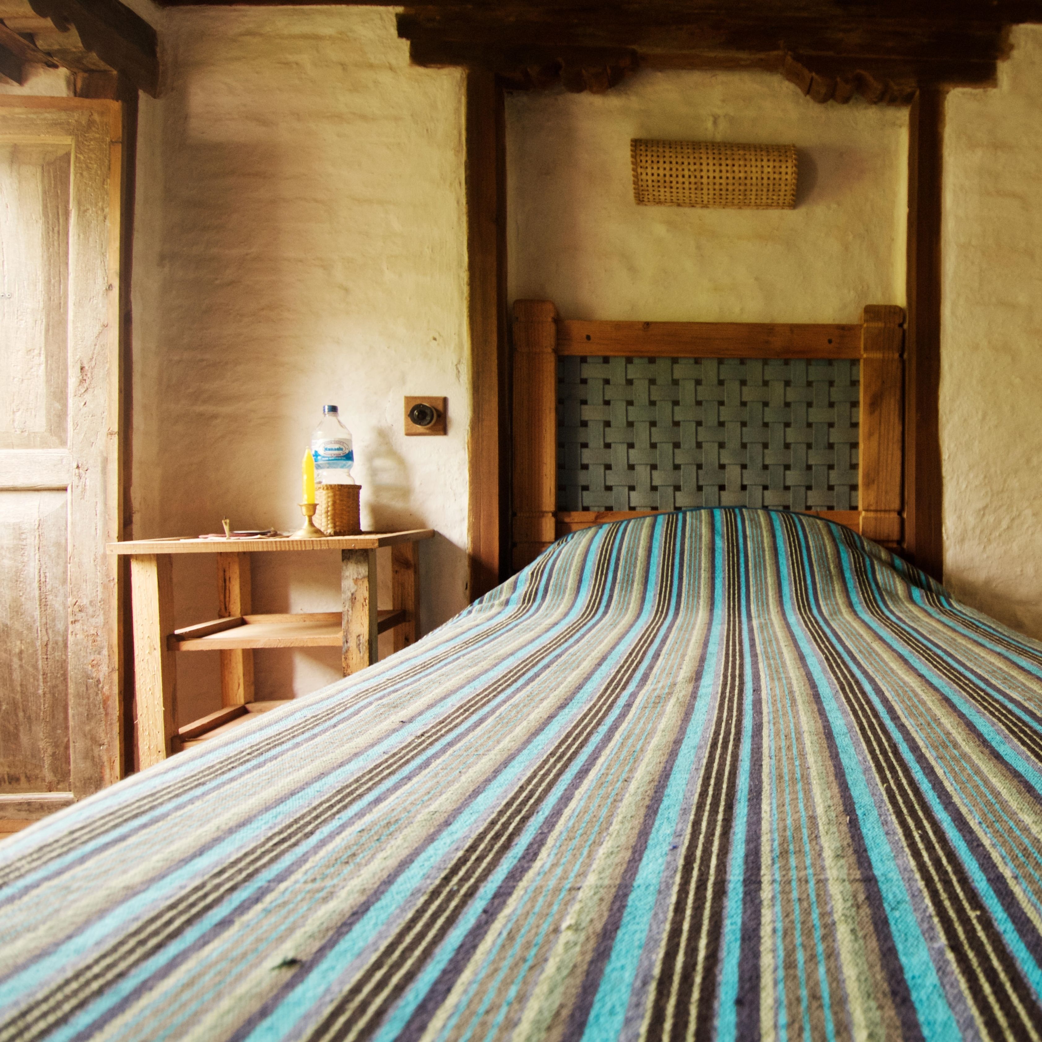 Una habitación con cama, cabecero de madera, una mesita con una botella de agua y una lámpara de pared.