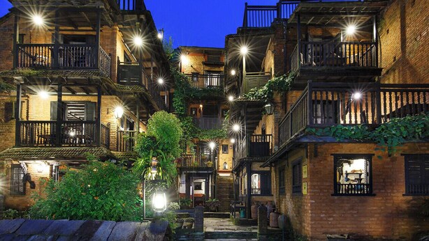 A narrow alleyway flanked by multi-story buildings with balconies, underlit by street lamps. - The Old Inn (Bandipur)