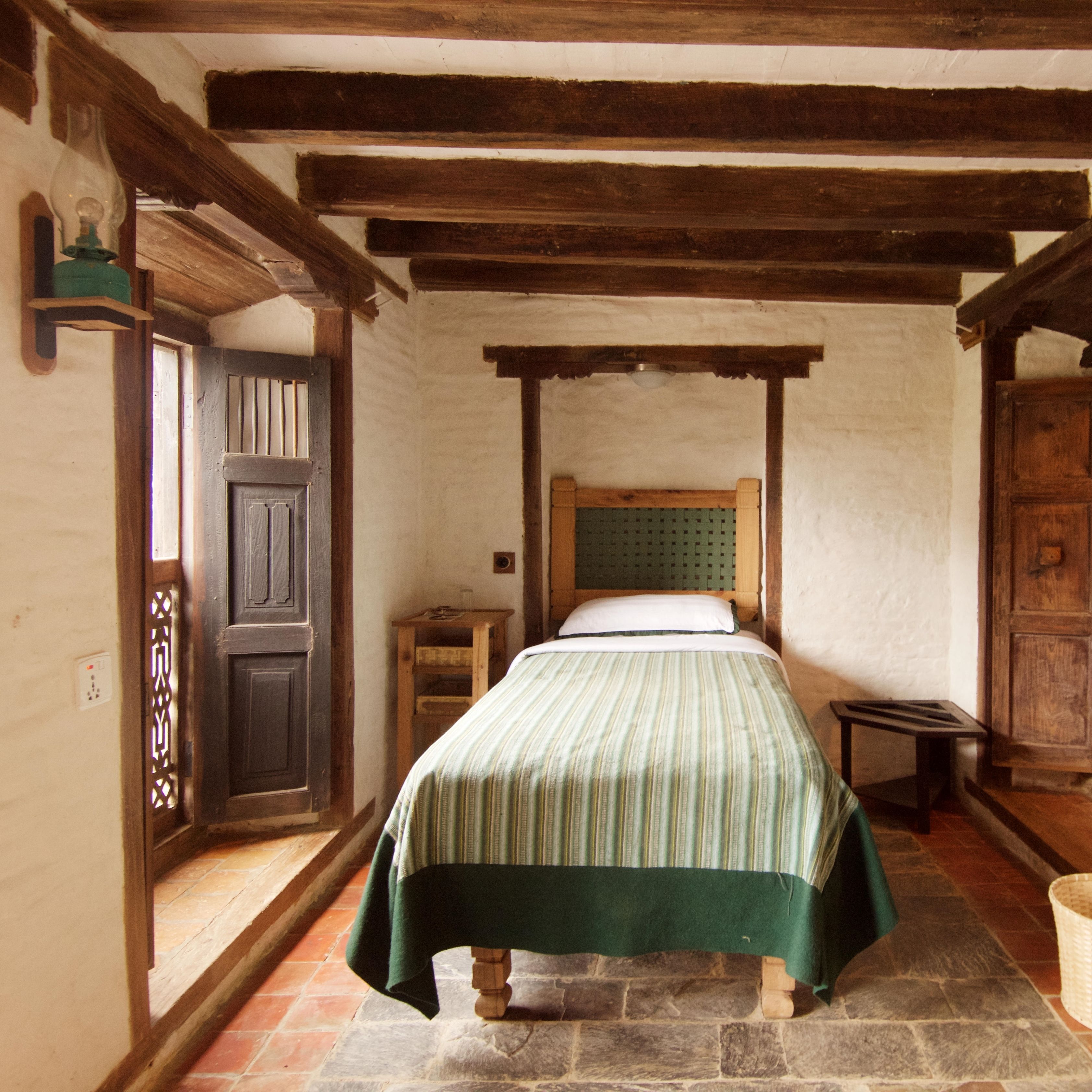 A traditional room with a bed, wooden beams, a stone floor, and a door with a decorative pattern.