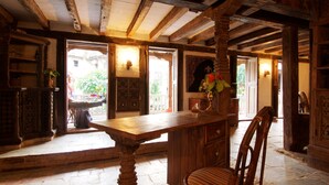 A rustic dining area with a wooden table and chairs, a bookshelf, and a view of the outside. - The Old Inn (Bandipur)