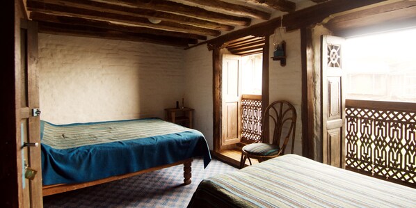 A room with two beds, wooden beams on the ceiling, a chair, and a window with a lattice design.