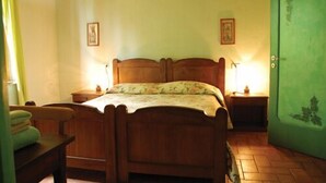 A bedroom with a wooden bed, two bedside tables, a green door, and two wall-mounted lamps. - Agriturismo Cascina degli Ulivi (Novi Ligure)