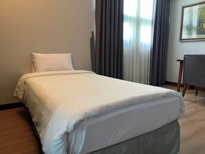 Una cama bien hecha en una habitación de hotel, con un cabecero y un sillón grises, y un cuadro en la pared.