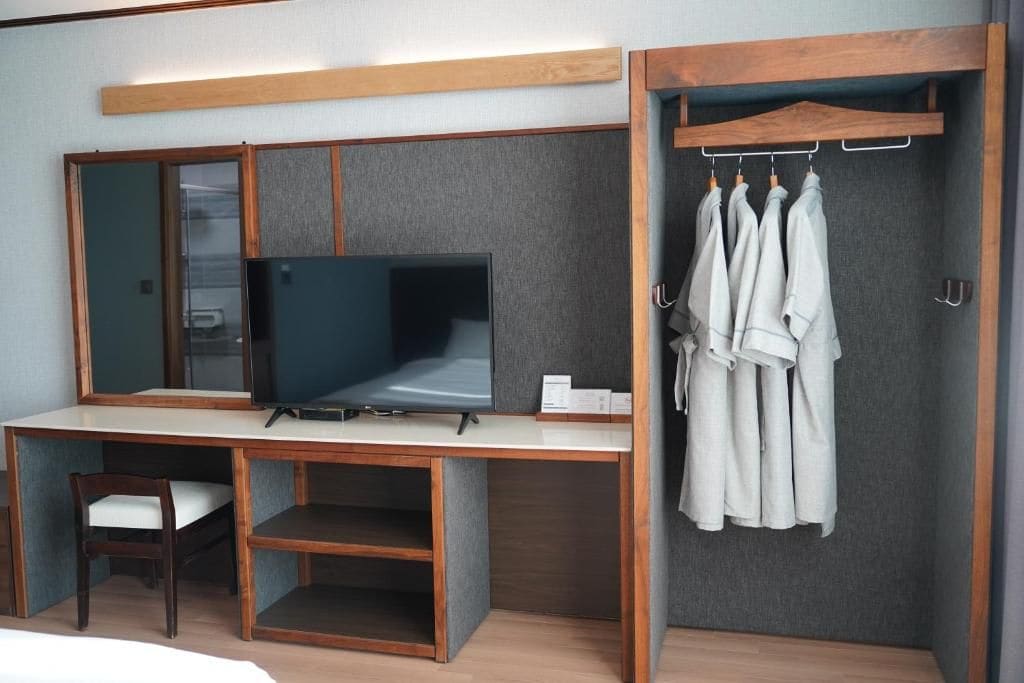 Une chambre d’hôtel équipée d’un bureau en bois, d’une télévision, d’une chaise, d’une armoire et d’un porte-vêtements.